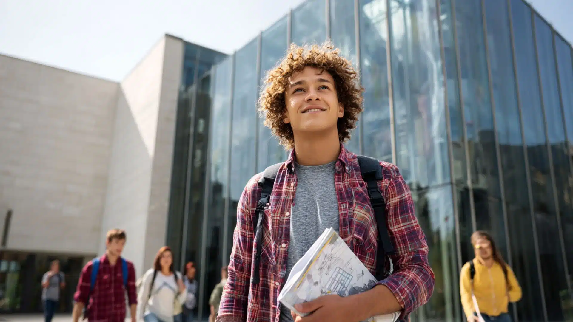 high school student with curly hair holding notebooks and a backpack, looking up confidently at a university campu