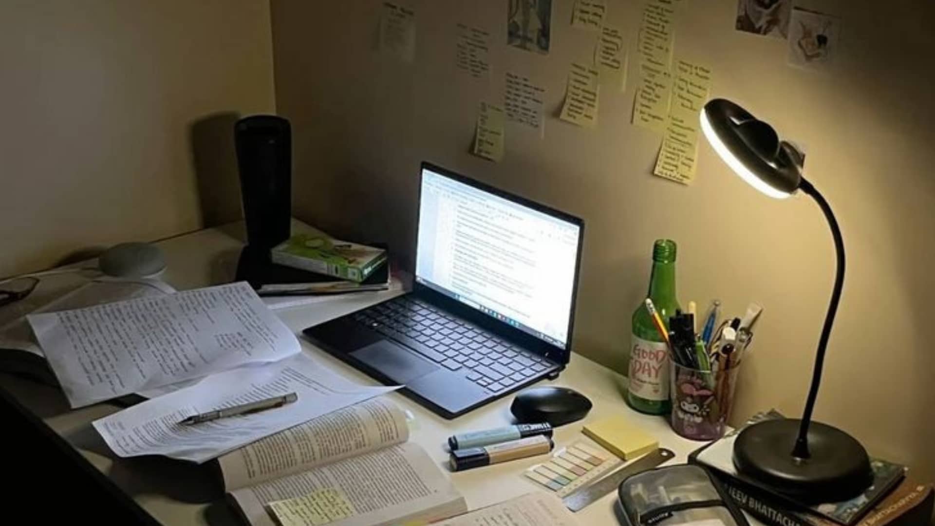 Late-night student study desk setup with laptop, open textbooks,  handwritten notes, spiral notebook, desk lamp glowing warmly,  stationery organizer, sticky notes on wall, and photos pinned  abov (1)