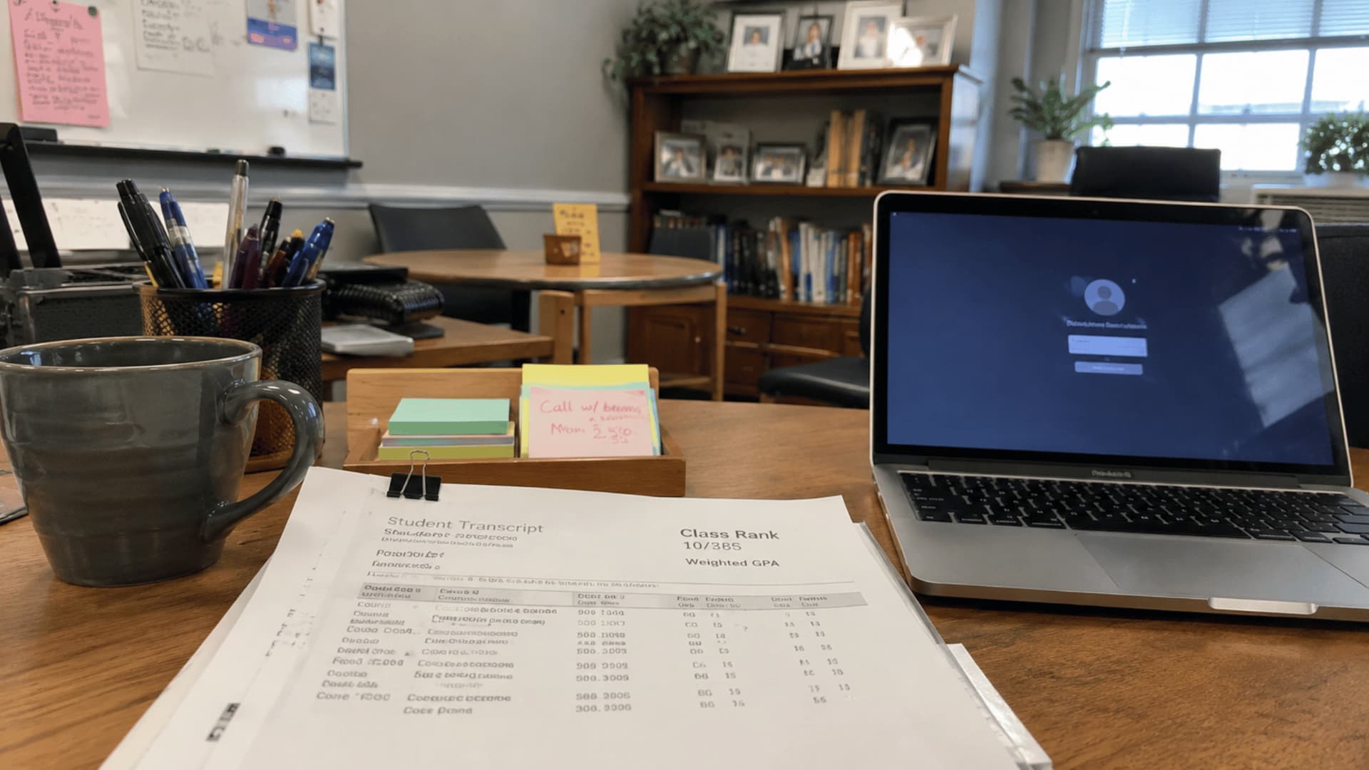 student transcript showing class rank beside a laptop, coffee mug, pens, and notes