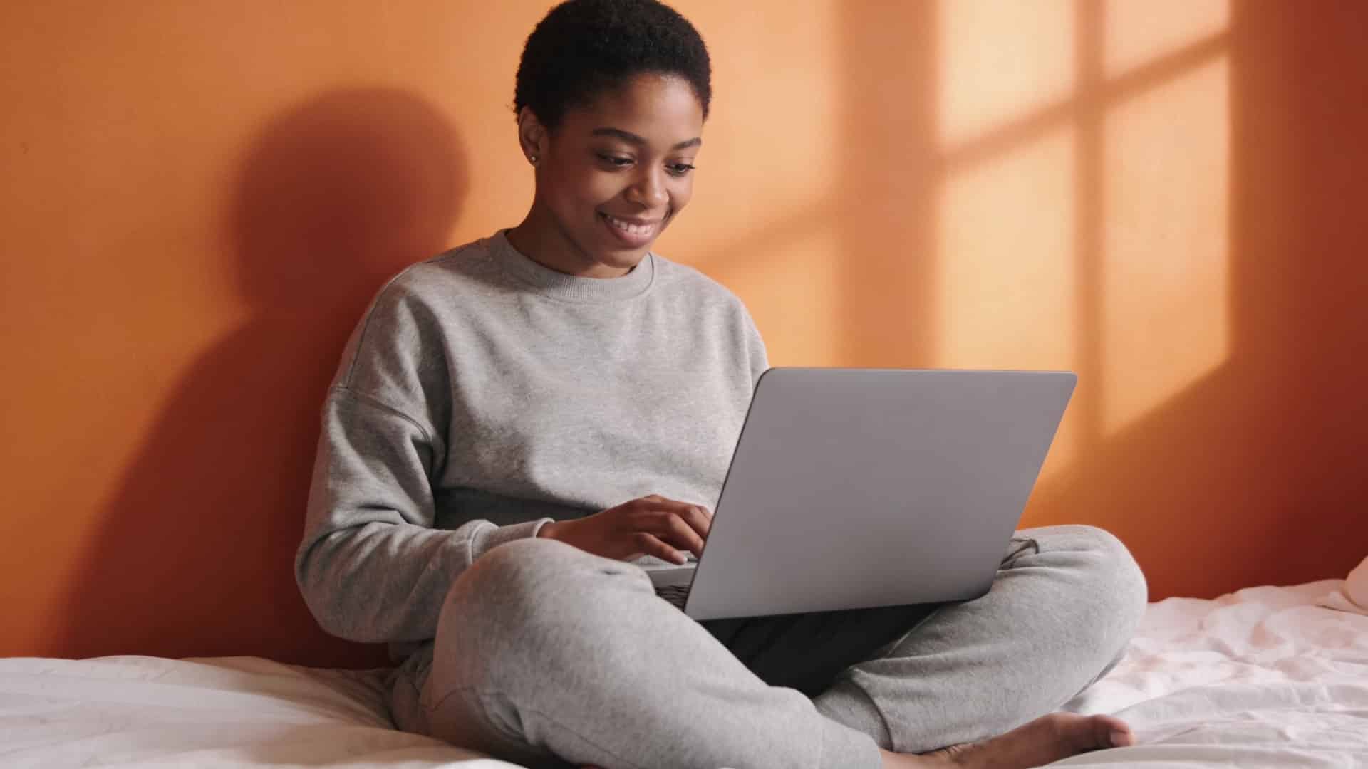 student sitting on a bed using a laptop while studying in a bright, comfortable room
