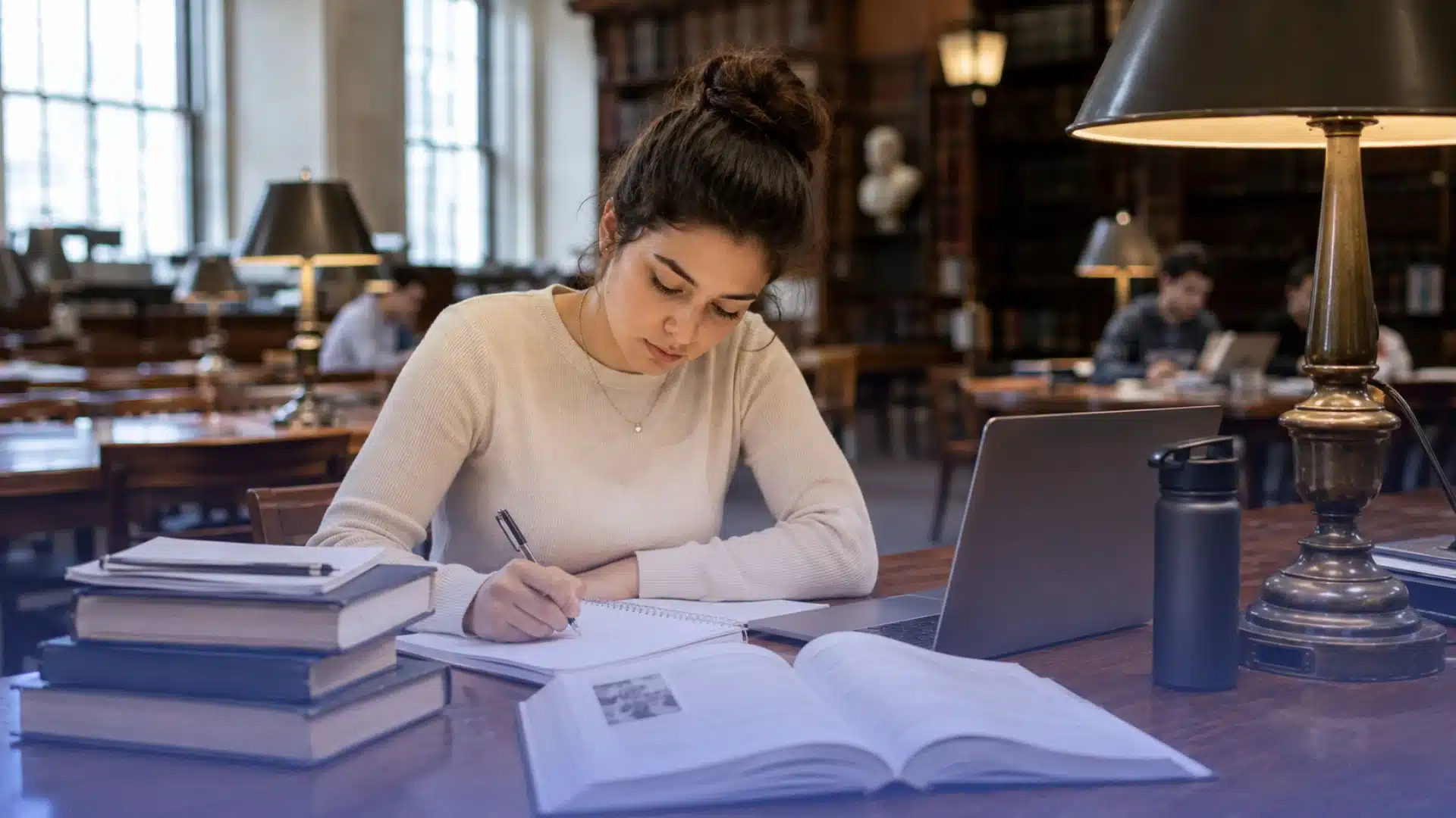 young medical student studying at a library desk with books and laptop in a quiet academic setting indoors today