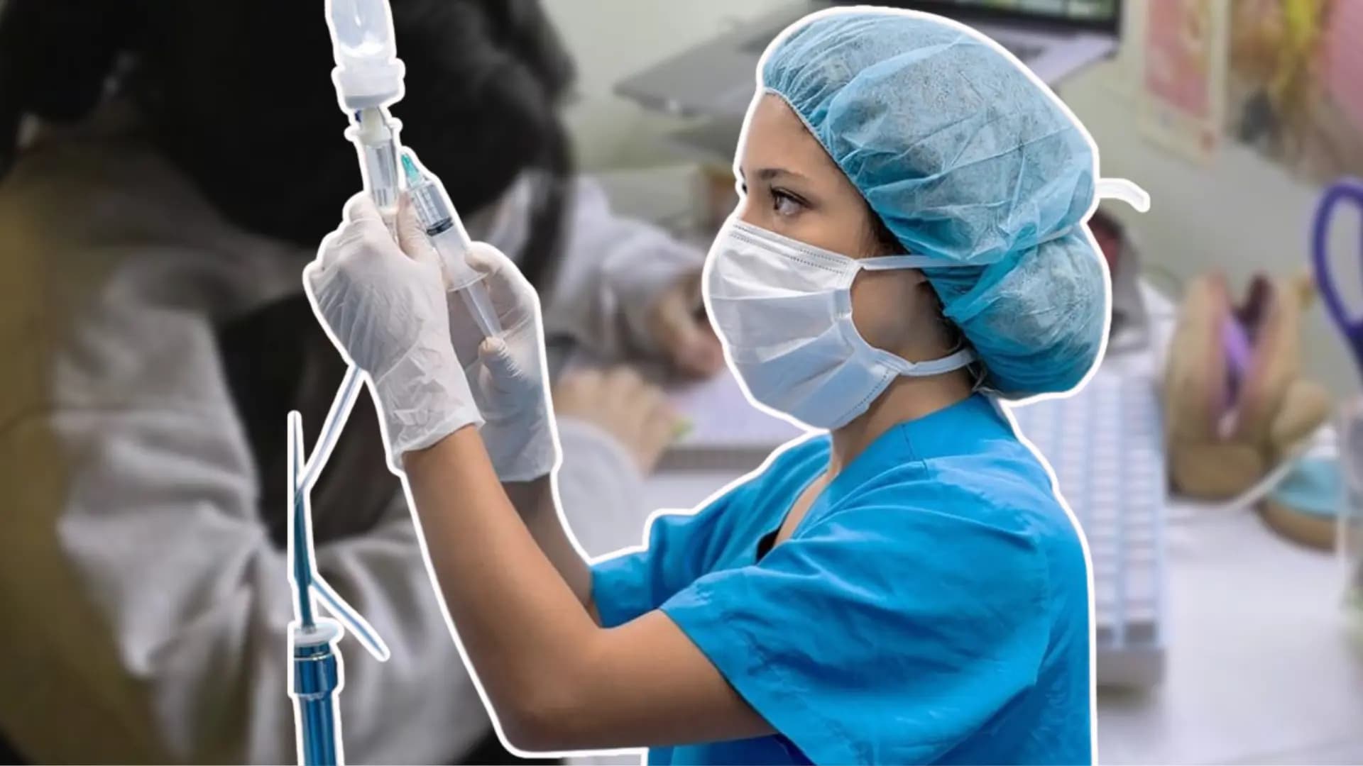 a masked healthcare worker in blue scrubs and a hair cap prepares an intravenous drip while wearing gloves